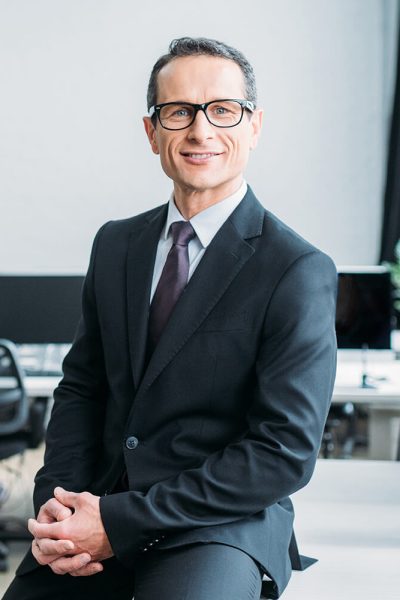 smiling-businessman-in-eyeglasses-sitting-on-table-V5AWVKC.jpg